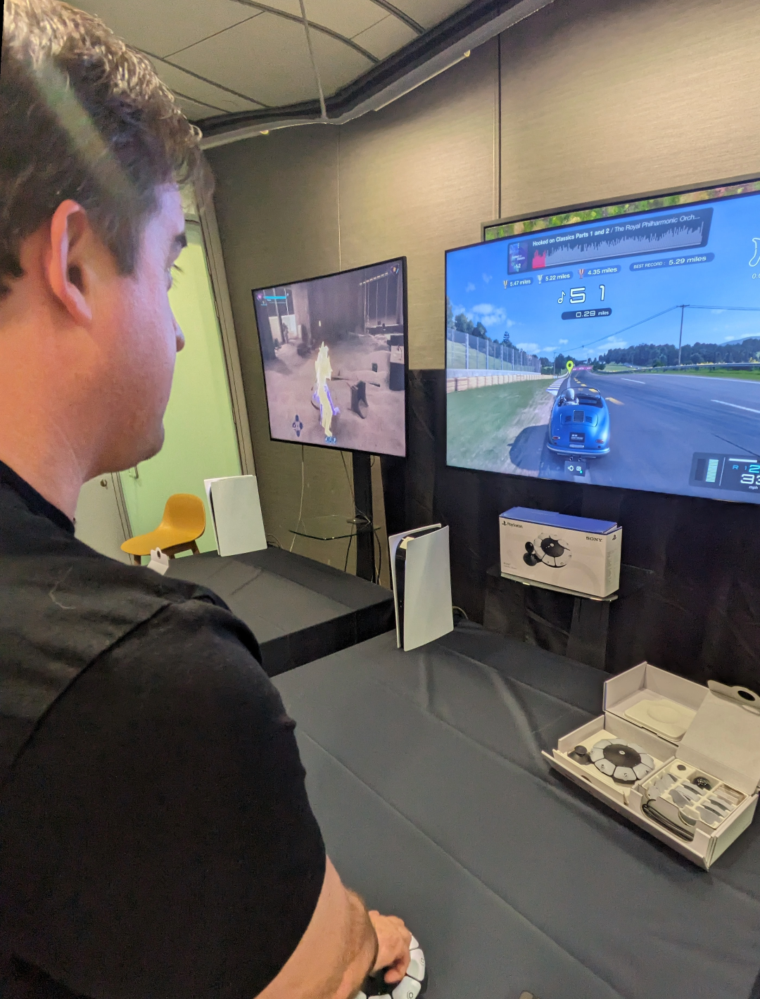 Chris stands in front of a screen displaying a game - he is using Sony's new Access controller, which is a circular controller with buttons around the edge