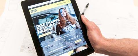 A hand holding a tablet with the Zuto homepage showing on the screen.