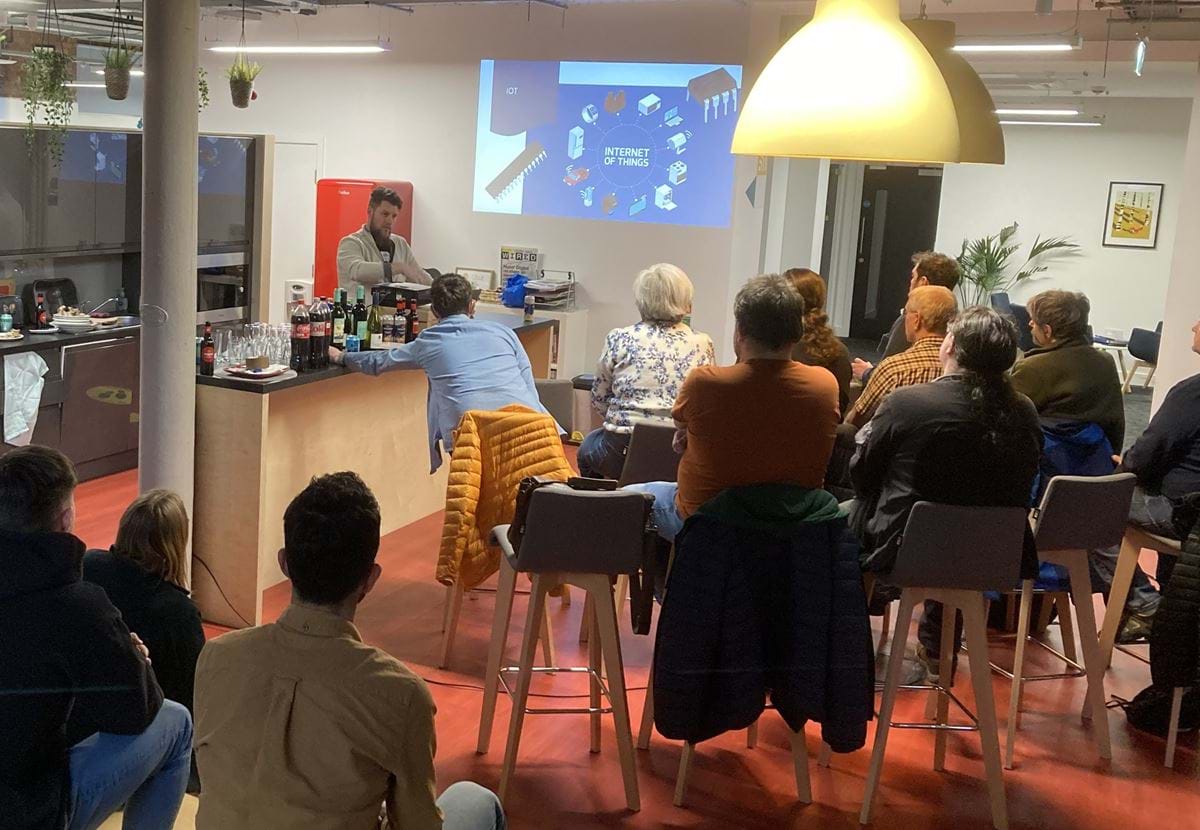 A group of people seated in the Nexer offices. They're watching a person stood presenting a slide.