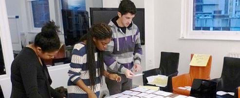 Three people standing around a desk arranging cards with words on them.