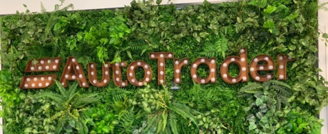 Brown metal signage of the Auto Trader logo, displayed on a leafy green background