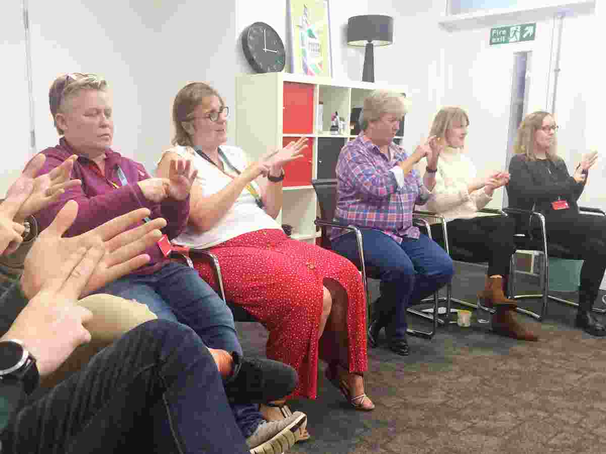 Five white people with their hands raised learning how to sign 