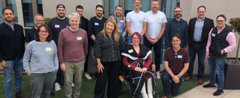 Accessibility roundtable attendees stand on a roof terrace - they're all smiling at the camera