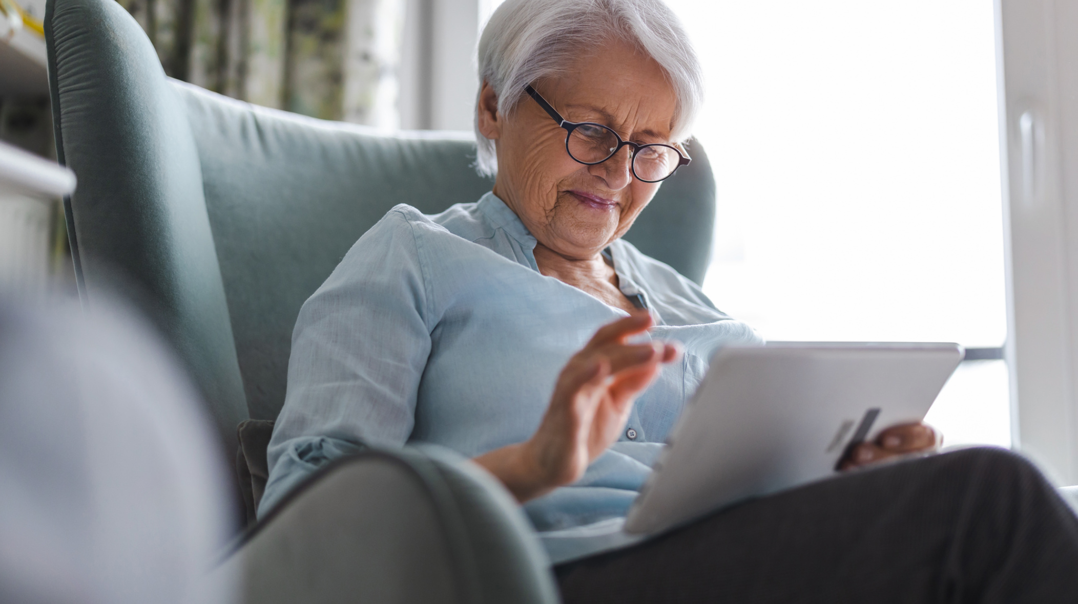 An elderly person smiles while using a tablet 