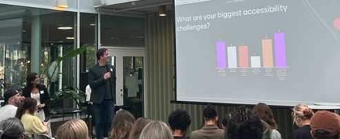 Chris stands in front of an audience of seated people, holding a microphone. On a screen is a slide reading 'What are your biggest accessibility challenges?', and the results of a Menti survey.
