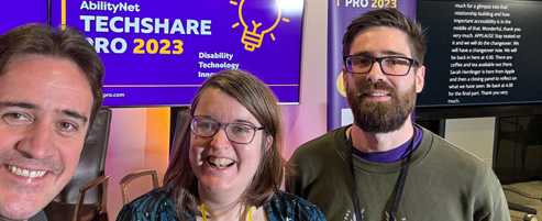 Chris, Emma and Danny from Nexer's accessibility team take a smiling selfie in front of the TechShare Pro 2023 banner