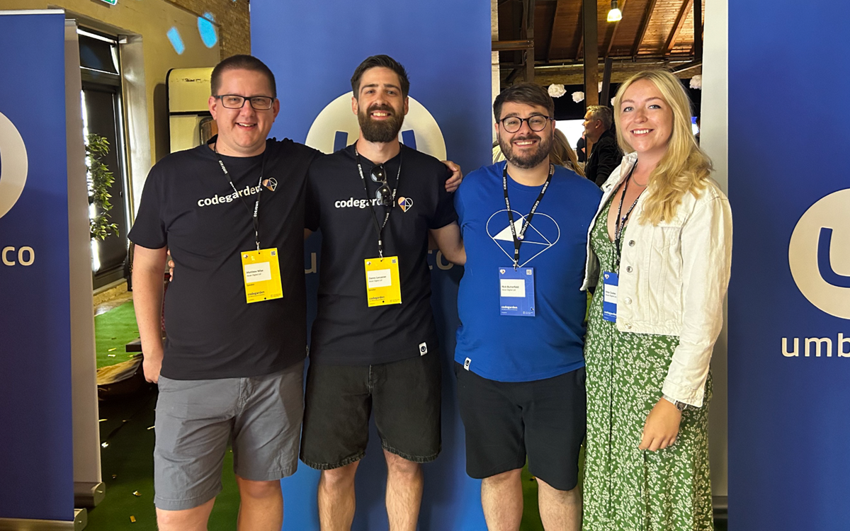 Matt Wise, Danny Lancaster, Rick Butterfield and Amy Czuba stand smiling in front of Umbraco branded roll up banners