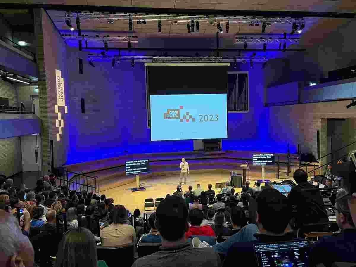 Shaun stands in the RNCM Concert Hall in front of a large audience, with the Camp Digital 2023 slide onscreen
