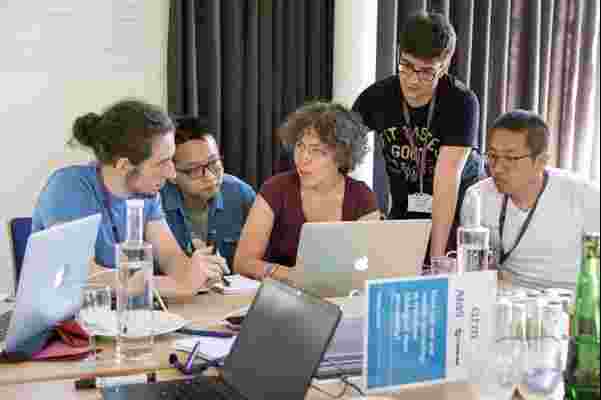 Five people grouped around a laptop, at a table. 