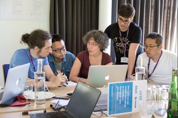 Five people grouped around a laptop, at a table.