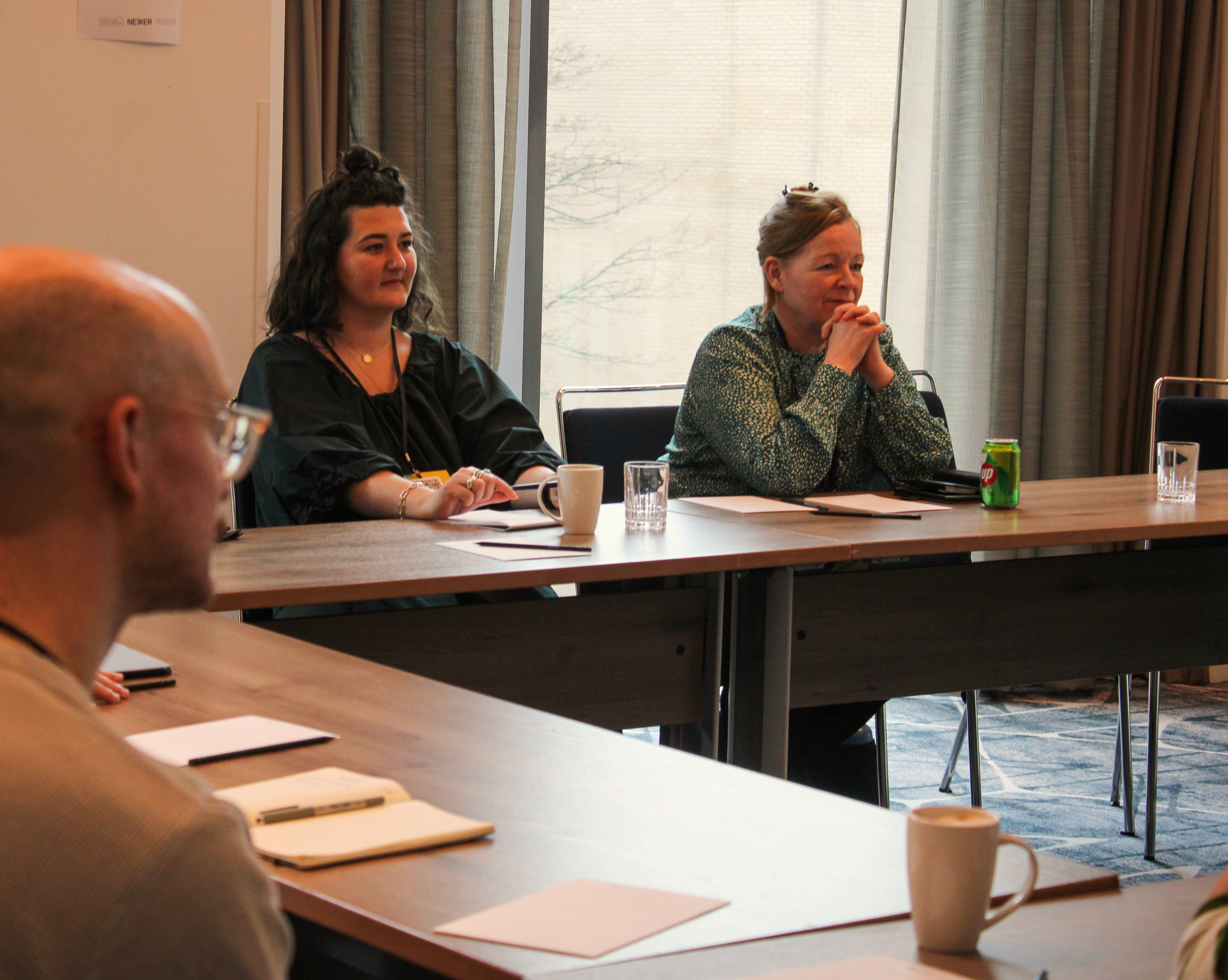 Unconference attendees sit around a table with drinks and a pen and pad in front of them