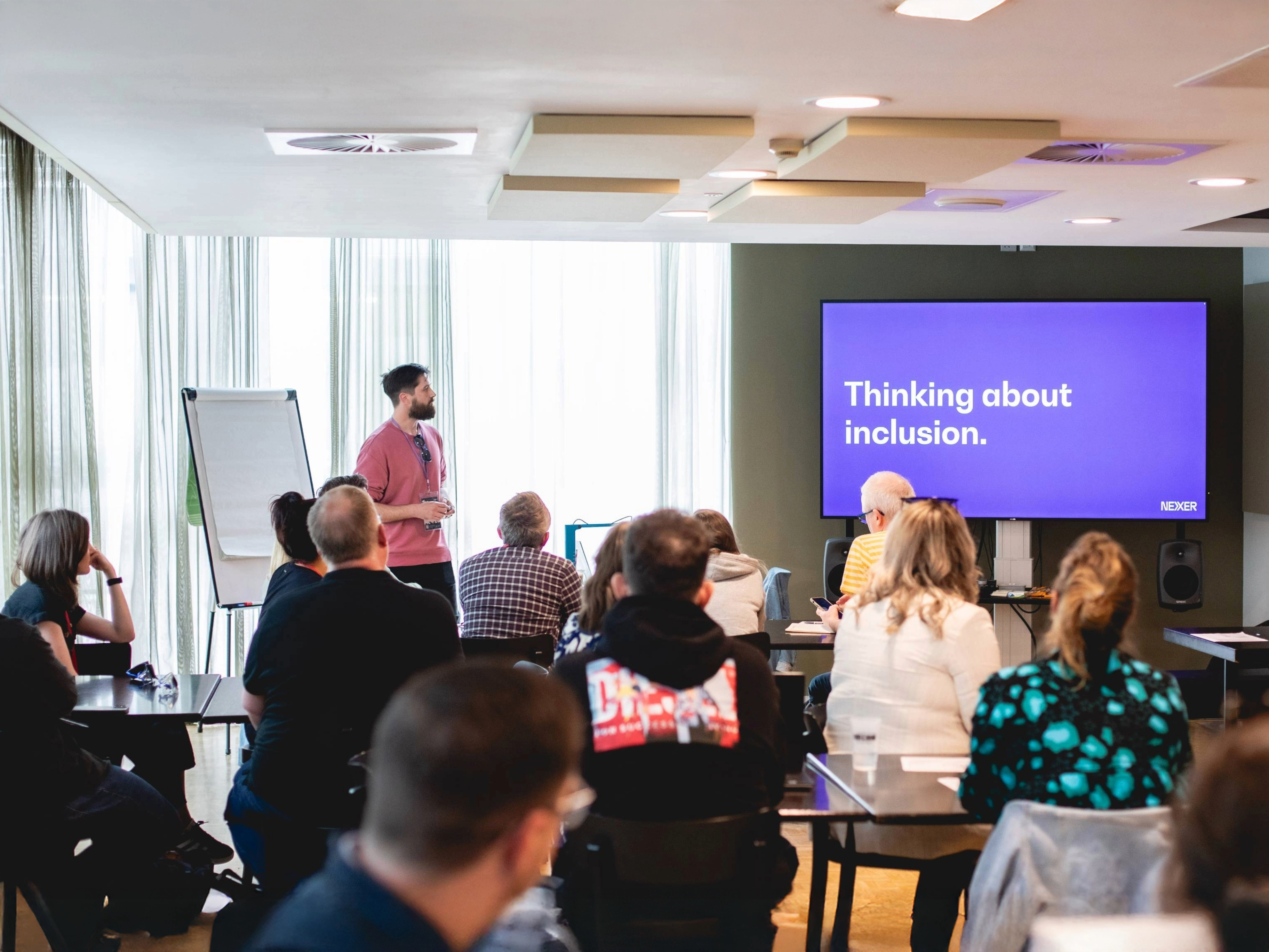 Danny Lancaster stands in front of a room of seated people. Onscreen a slide reads 'Thinking about inclusion'
