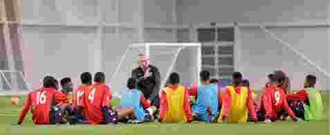 A group of football players sat on the pitch listening to their coach