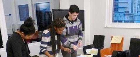 Two black women and one white man leaning over a table with cards spread over it.
