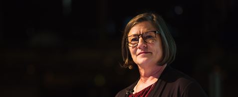 Dana Chisnell. A white woman with short brown hair and glasses. She is wearing a necklace and a maroon top. Her head is tilted to the side and she looking thoughtful.
