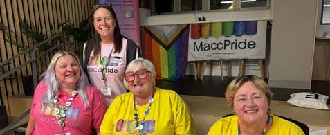 Four members of the Macc Pride team sit on the steps at the Nexer office. In the background are Macc Pride banners.