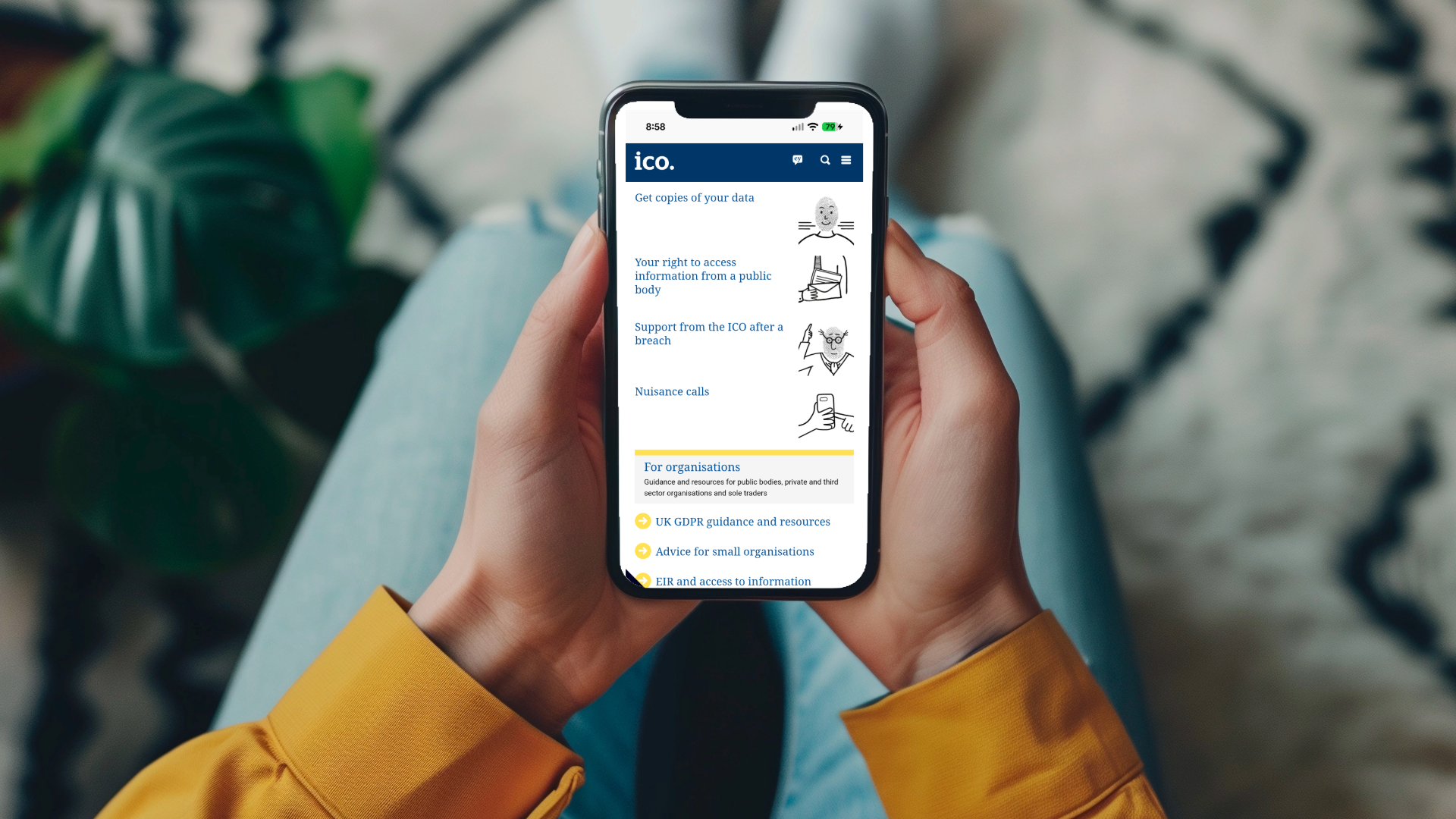 A pair of hands holding a mobile phone with the ICO homepage displayed.