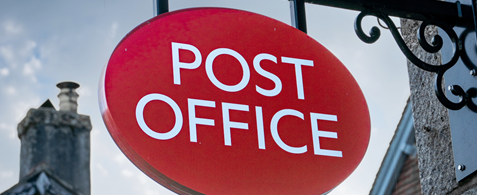 A Post Office sign, with blue sky visible behind it