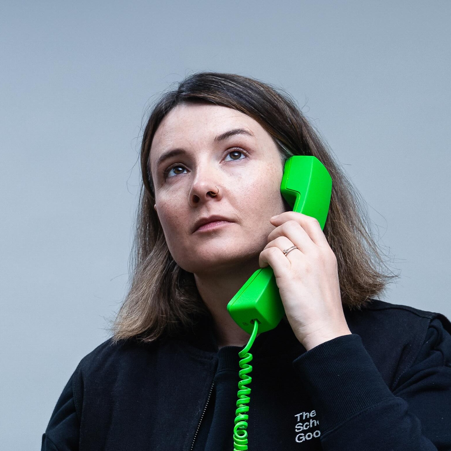Studio portrait of Sarah Drummond holding a bright green telephone handset to one ear against a pale background.