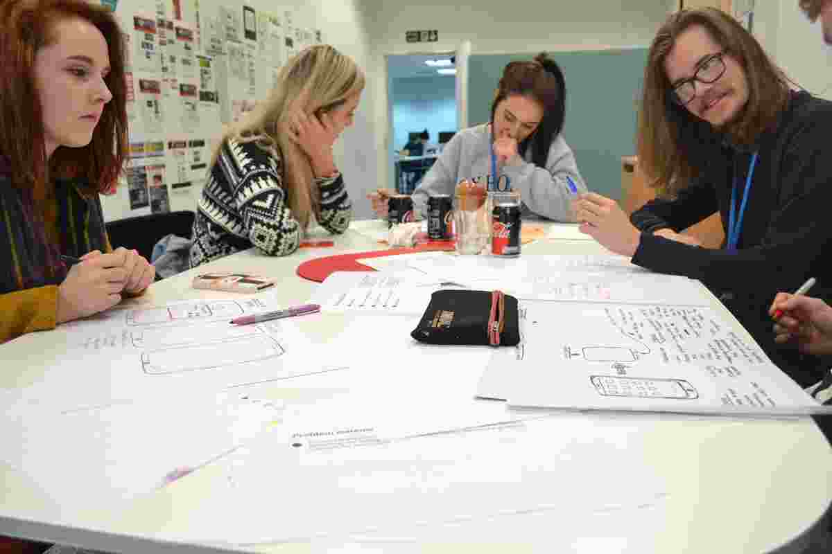 Four white people sat around a table, working and writing on paper. 