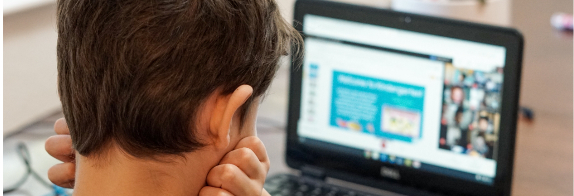 Boy looking at a laptop screen and holding his chin in his hands, his face is turned away only the back of his head is visible