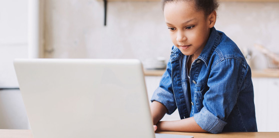 A girl is sitting facing the camera, looking at a laptop screen.