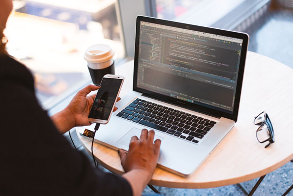 Person in front of computer typing on mobile phone.