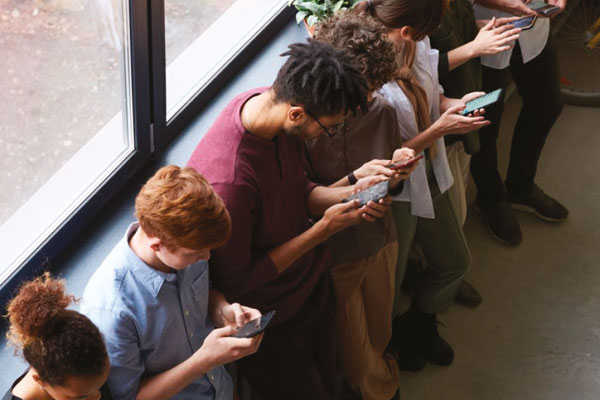 People stood against a wall all on their phones.